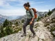 Best Women’s Hiking Boots for Every Foot Shape Woman in Merrell hiking boots descending a rocky mountain trail with a loaded daypack