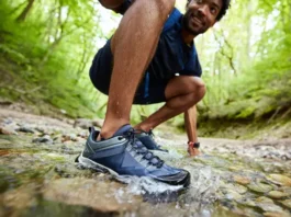 A male hiker steps through a clear stream, showcasing waterproof hiking shoes with water beading off, illustrating their worth on wet trails.