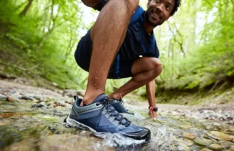 Are Waterproof Hiking Shoes Worth It? A 2025 Guide A male hiker steps through a clear stream, showcasing waterproof hiking shoes with water beading off, illustrating their worth on wet trails.