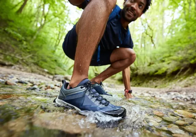 A male hiker steps through a clear stream, showcasing waterproof hiking shoes with water beading off, illustrating their worth on wet trails.