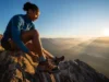 The Science of Boot Socks: A Guide for Serious Hikers A female hiker adjusts her hiking boot and technical boot sock while pausing on a mountain overlook with a stunning view at sunrise.
