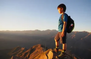 Field-Tested: The Best Hiking Boots for Young Hikers A young child in hiking boots stands on a mountain summit at sunset, looking out over a beautiful valley, embodying the spirit of adventure.