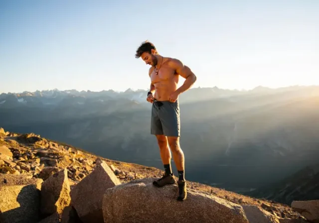 A hiker stands on a mountain peak, looking down at his technical men's hiking shorts, representing a data-backed analysis of the best gear for the trail.
