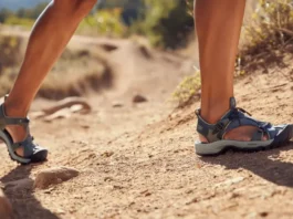A female hiker compares a zero-drop hiking sandal on one foot with a high-drop hiking sandal on the other, illustrating the choice between footwear philosophies for women.