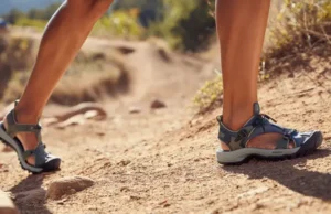 Women’s Hiking Sandals: Zero vs. High Drop? A female hiker compares a zero-drop hiking sandal on one foot with a high-drop hiking sandal on the other, illustrating the choice between footwear philosophies for women.