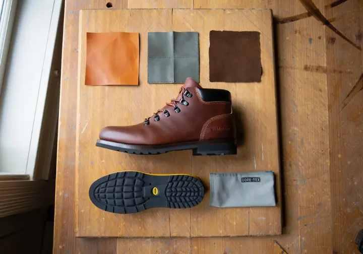 An expert's guide to boot materials, showing a leather hiking boot on a workbench alongside swatches of full-grain, nubuck, and suede leather, a Vibram sole, and GORE-TEX fabric.