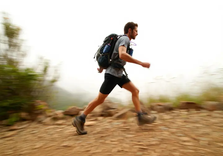 A hiker tests the stability and comfort of a hydration pack while moving quickly over a challenging, rocky trail.