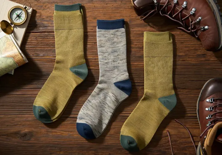 A flat-lay photo showing three pairs of the best hiking boot socks for 2025 arranged next to hiking boots and a map.
