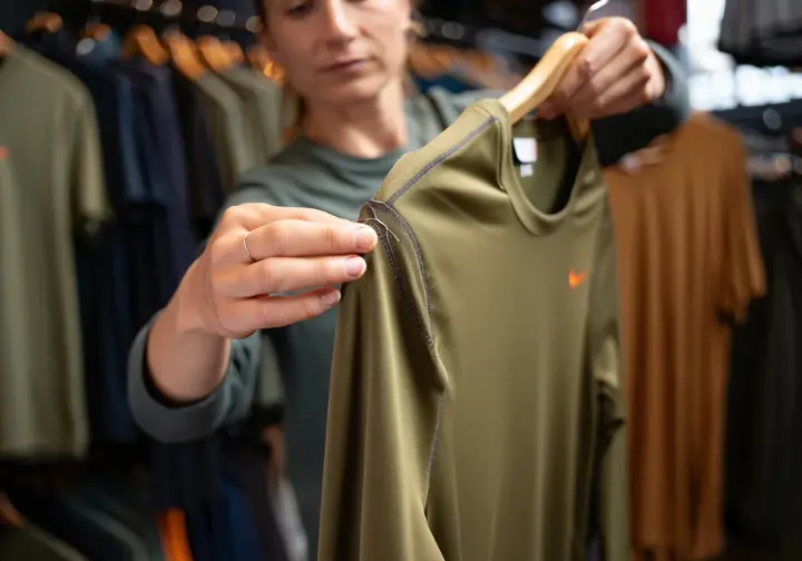 A close-up of a woman's hands inspecting the flatlock seam on a technical hiking shirt, a final consideration to avoid mistakes before buying.
