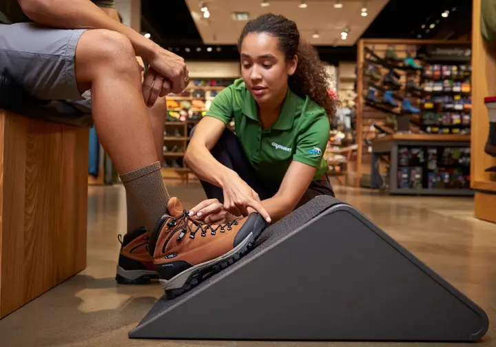 A practical guide to selecting men's leather hiking boots, showing a customer being professionally fitted by a store expert in an outdoor gear shop.
