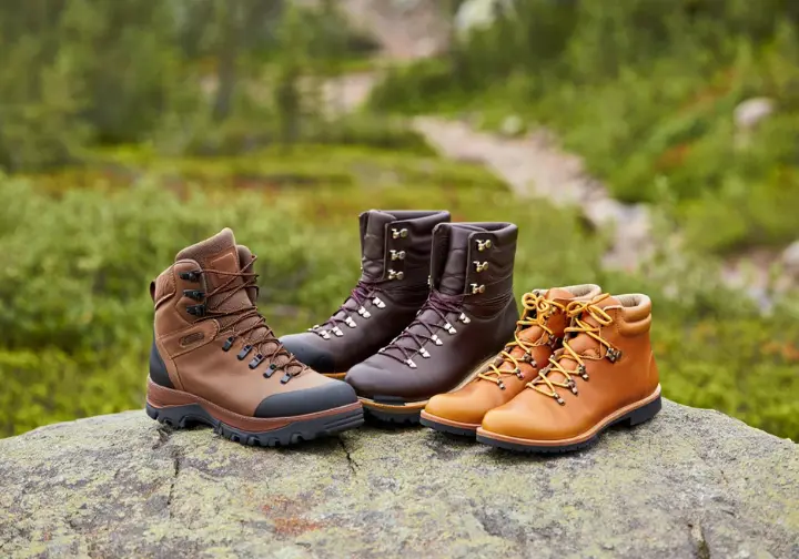 Summit selections of the best men's leather hiking boots, featuring three different styles for backpacking and hiking, displayed on a rock on a mountain trail.