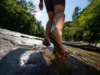 Trail-Tested: Best Barefoot Hikers for Rock & Mud A hiker's feet in minimalist barefoot boots confidently navigating a trail that transitions from wet rock to deep mud, symbolizing the decision framework for choosing the right footwear.