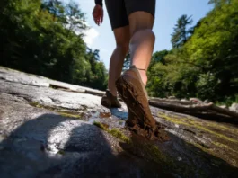 A hiker's feet in minimalist barefoot boots confidently navigating a trail that transitions from wet rock to deep mud, symbolizing the decision framework for choosing the right footwear.