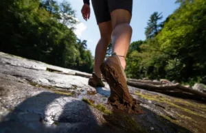 Trail-Tested: Best Barefoot Hikers for Rock & Mud A hiker's feet in minimalist barefoot boots confidently navigating a trail that transitions from wet rock to deep mud, symbolizing the decision framework for choosing the right footwear.