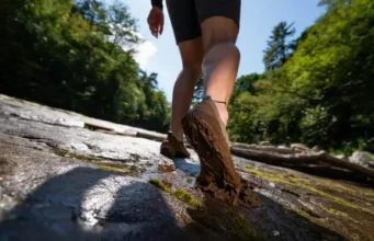 Trail-Tested: Best Barefoot Hikers for Rock & Mud A hiker's feet in minimalist barefoot boots confidently navigating a trail that transitions from wet rock to deep mud, symbolizing the decision framework for choosing the right footwear.