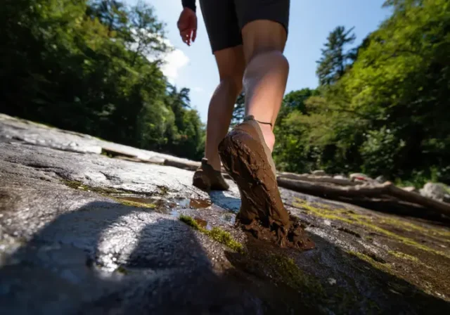 A hiker's feet in minimalist barefoot boots confidently navigating a trail that transitions from wet rock to deep mud, symbolizing the decision framework for choosing the right footwear.