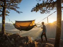 A hiker enjoys a morning coffee next to their field-tested hammock tent, set up on a mountain overlook at sunrise.