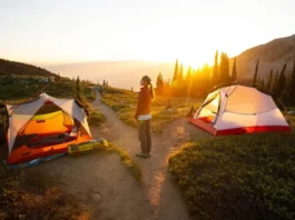 A hiker stands at a fork in a mountain trail at sunset, deciding between a lightweight Marmot Tungsten tent and a durable Big Agnes Blacktail tent pitched on separate paths.
