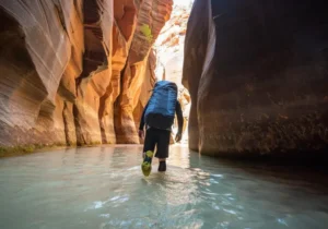A prepared hiker wearing specialized hiking water shoes wades through the Virgin River in the magnificent slot canyon of The Narrows, Zion National Park.