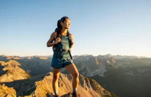 The Pro Hiker’s Guide to Women’s Hiking Shorts A female hiker wearing functional hiking shorts stands on a mountain summit at golden hour, looking out over a vast mountain range.