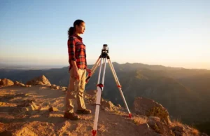 Steel Toe Hiking Boots: A Field-Tested Buyer’s Guide A land surveyor in steel toe hiking boots stands with her professional equipment on a scenic mountain trail, embodying the focus of this field-tested buyer's guide.