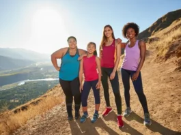 A diverse group of four women hikers with different body types standing confidently on a mountain summit, all wearing well-fitting hiking pants.