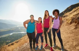 Top Hiking Pants for Women: Tested for All Body Types A diverse group of four women hikers with different body types standing confidently on a mountain summit, all wearing well-fitting hiking pants.