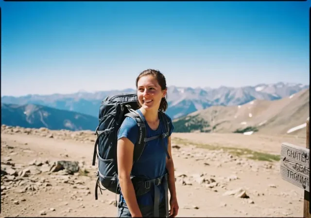 A woman wearing a well-fitted women's hiking pack smiles confidently while pausing on a sunny mountain trail.