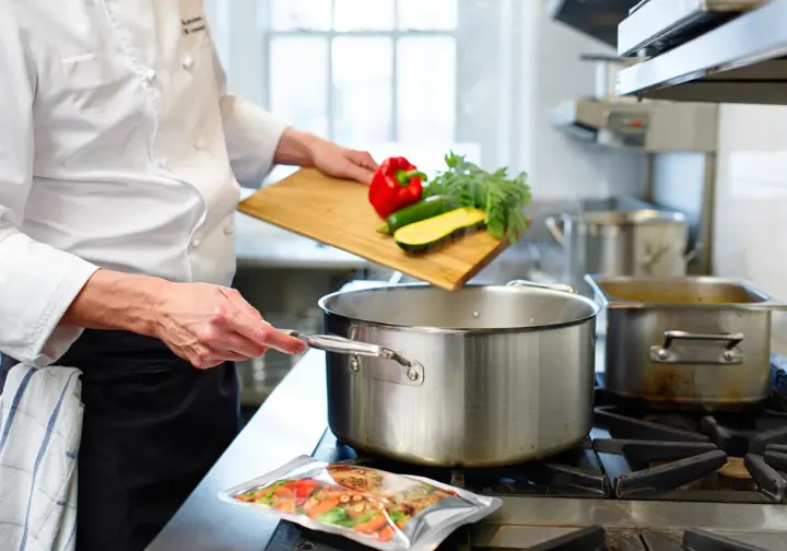 A chef meticulously prepares food in a professional kitchen, with a Good To-Go meal pouch nearby, illustrating the chef-driven philosophy behind the hiking food.