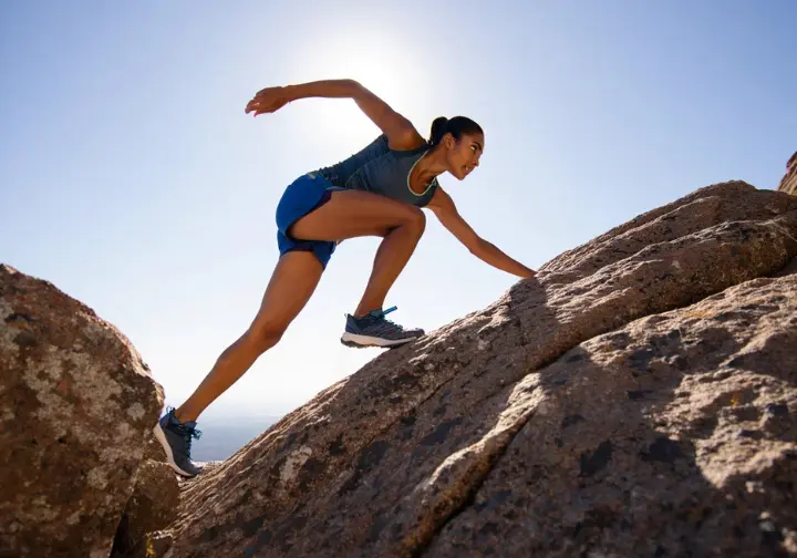 A female hiker tests the durability and stretch of her hiking shorts while scrambling up a steep and rocky mountain trail.