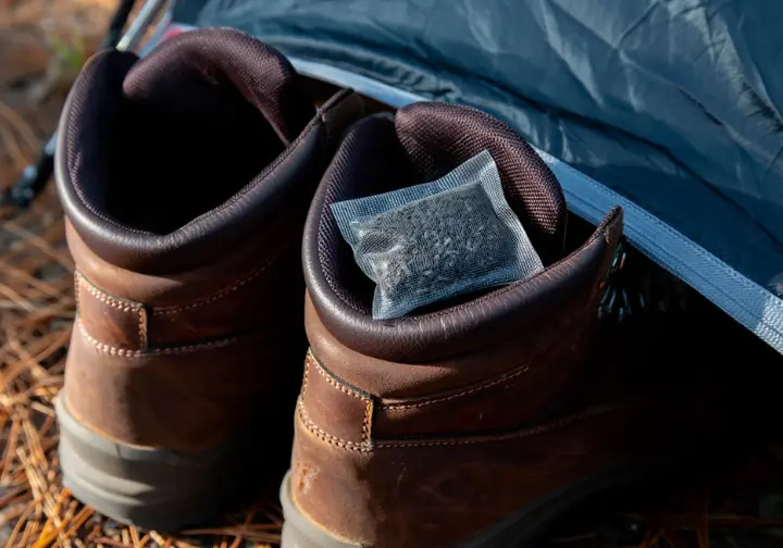 A small sachet of activated charcoal inside a hiking boot at a campsite, demonstrating odor control for camping hygiene.