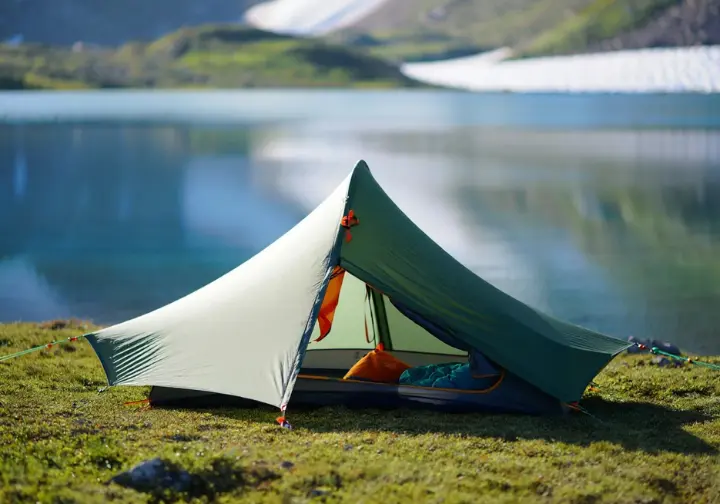 A top-rated 2-person backpacking tent is pitched perfectly at a campsite next to a serene alpine lake, showcasing one of the best tents of 2025.
