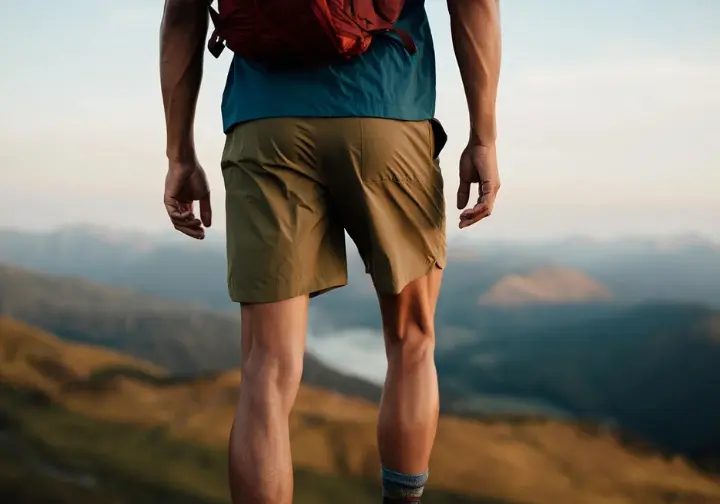 A confident hiker stands on a scenic mountain overlook, wearing one of the best men's hiking shorts of 2025, showcasing their excellent fit and features.