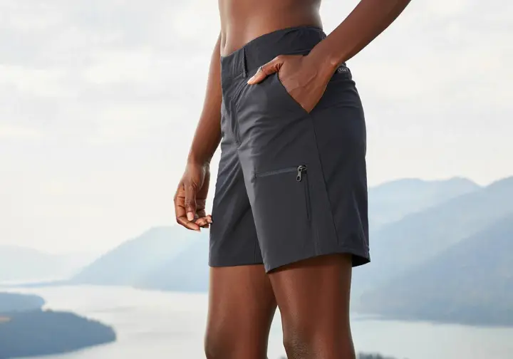 A hiker wearing a top-rated pair of women's hiking shorts smiles at a scenic mountain overlook, showcasing their excellent fit and design.