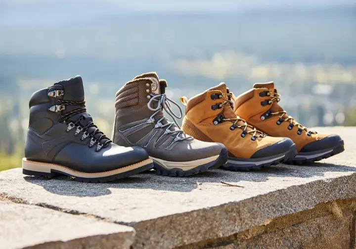 A curated lineup of the best steel toe hiking boots of 2024, displayed on a rock with a scenic mountain trail blurred in the background.