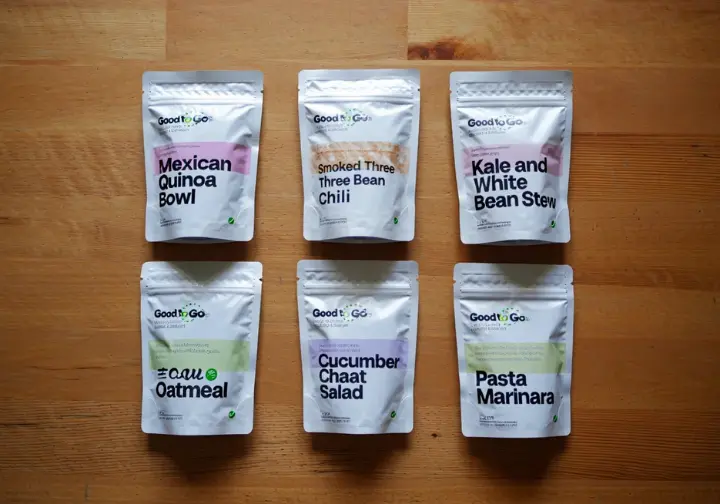 A flat lay of Good To-Go meal pouches, including Mexican Quinoa Bowl and Smoked Three Bean Chili, highlighting gluten-free, vegan, and nut-free options for hikers.