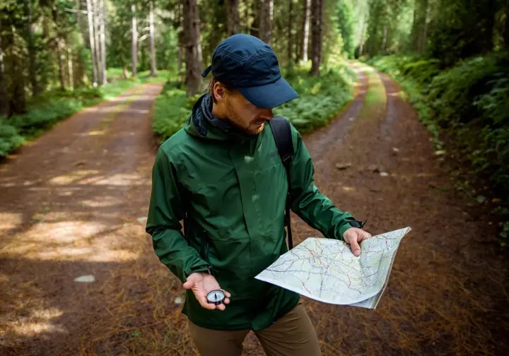 A hiker intently studying a map and compass at a trail junction, symbolizing the importance of judgment in hiking and avoiding common mistakes.