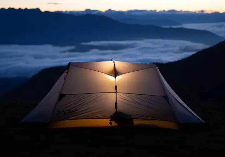 The Marmot Tungsten 2P, a top pick hiking tent, glows warmly on a mountain overlook at dusk, showcasing its ideal use for backpacking adventures.