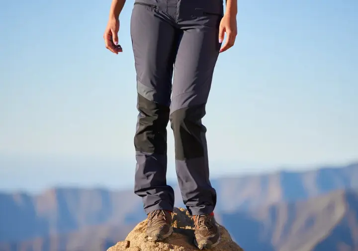 A confident woman hiker wearing a pair of the best women's hiking pants of 2025, posing on a mountain with a blurred background.