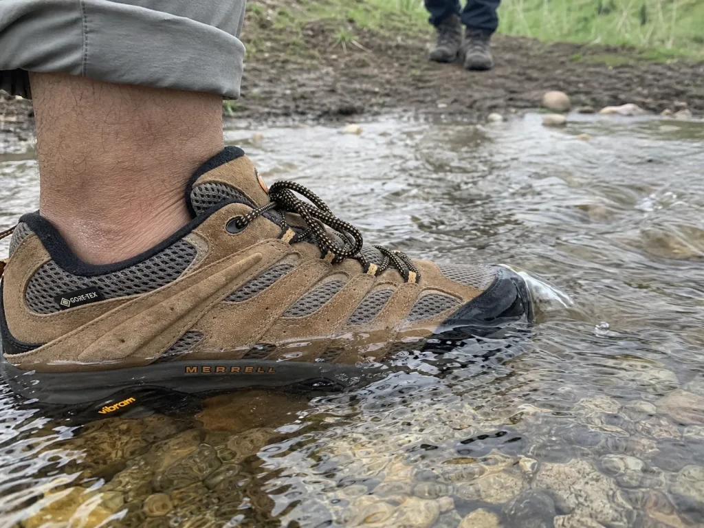 A waterproof hiking shoe at the edge of an ankle-deep creek crossing on a grey day