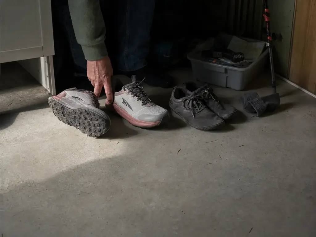 Cushioned hiking shoes and barefoot trail shoes side by side on a garage floor