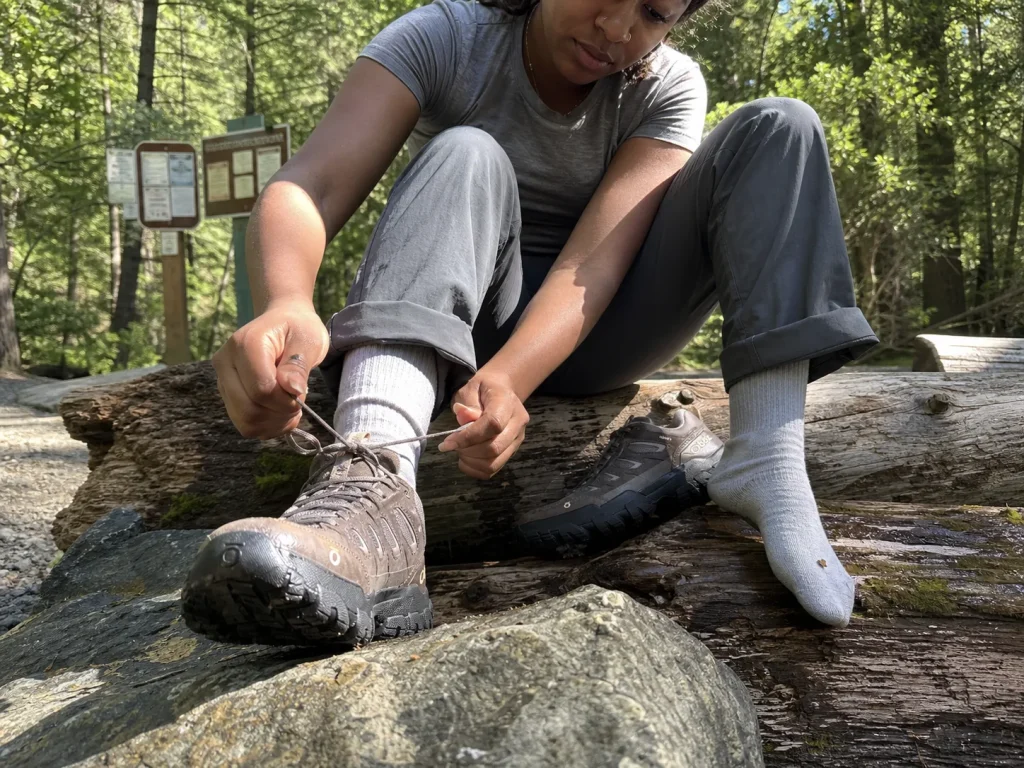 Woman tightening the laces of a wide-fit waterproof hiking shoe on a trailhead log