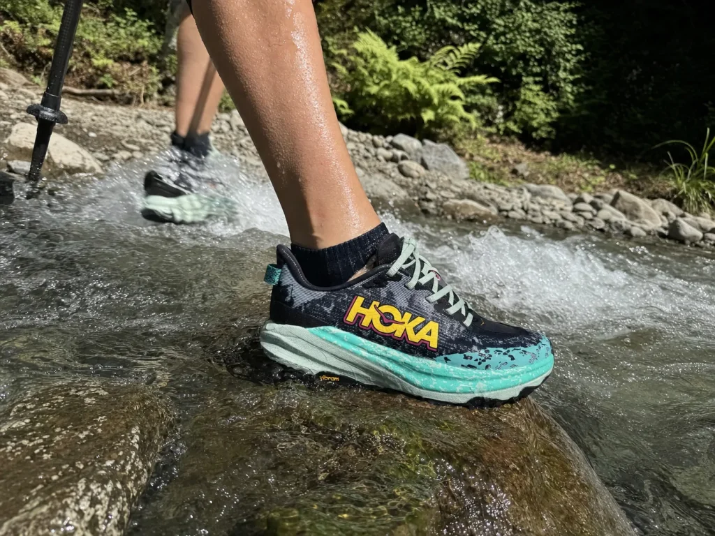Low-cut hiking shoe stepping into a shallow stream crossing with water near the collar