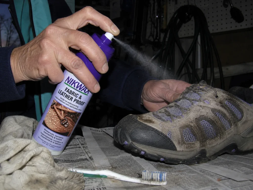 Spraying Nikwax waterproofing onto a hiking shoe on a workbench under harsh flash