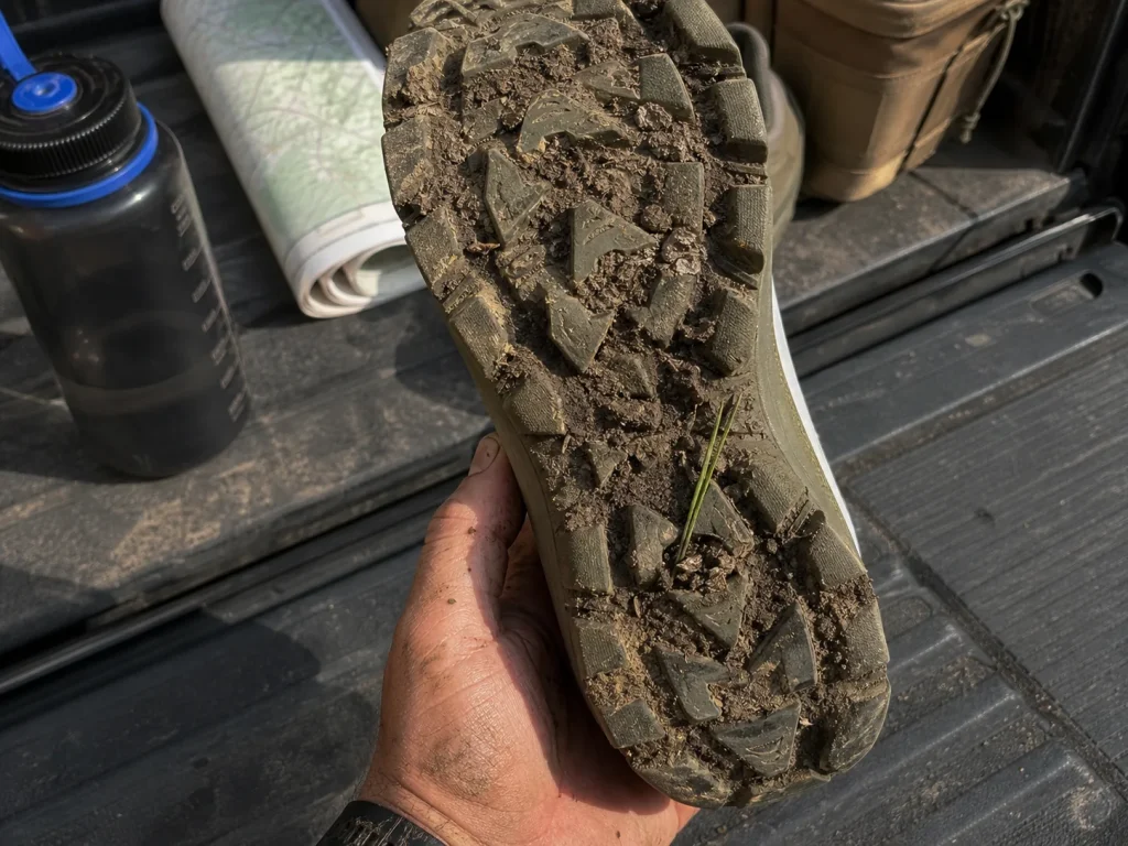 Overhead view of a muddy aggressive-lug outsole on a waterproof hiking shoe held up by hand