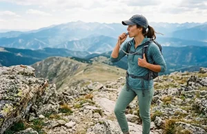 Best CamelBak Hydration Backpack for Every Hike Hiker drinking from a CamelBak hydration backpack hose on a sunlit ridgeline trail