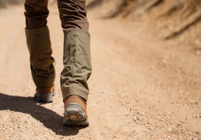 A hiker on a dusty trail wears mid-height gaiters, illustrating their function in preventing debris from entering boots, for a guide on hiking with gaiters.