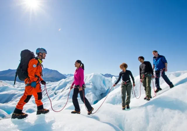 Diverse group of hikers on the Matanuska Glacier, led by a professional guide, illustrating the guided tour experience versus a self-guided walk.