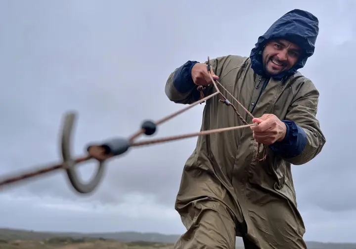 A hiker in full rain gear tensions a guyline to storm-proof their tent against a dramatic, overcast sky.
