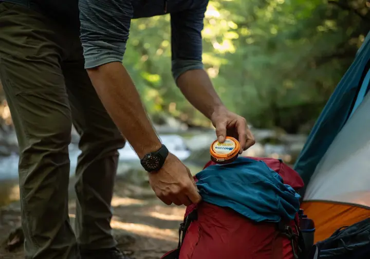 A backpacker at a forest campsite demonstrates outdoor ethics by properly securing their food in a bear canister.